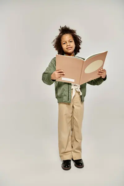 Une jeune fille avec un livre, captivée par les pages, debout sur un fond blanc. — Photo de stock