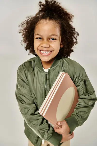 Молода афроамериканська дівчина в зеленій куртці бомбардувальника тримає книгу. — стокове фото