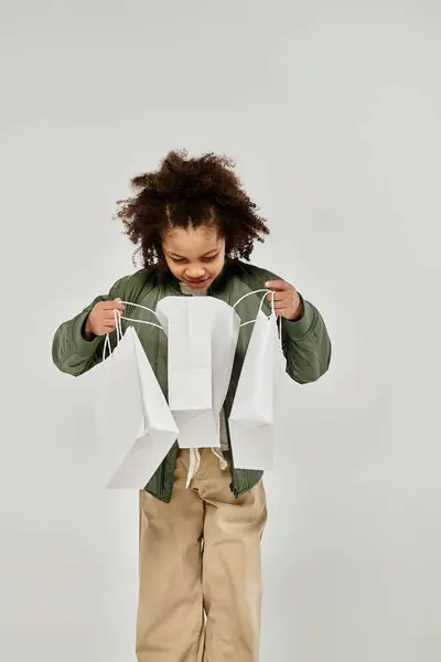 A young girl with curly hair holds colorful shopping bags against a white background. — Stock Photo