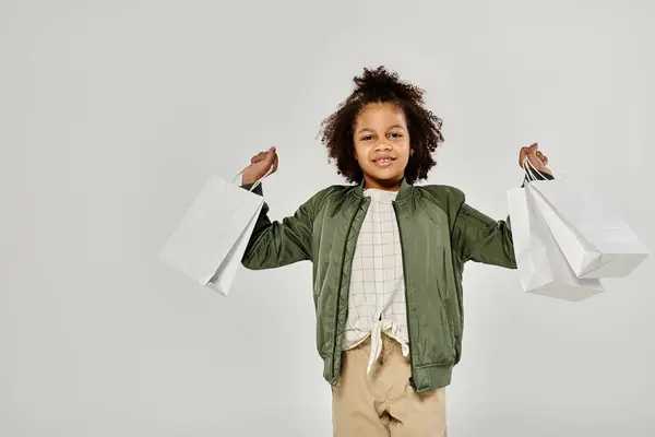 A stylish little girl with curly hair holding shopping bags in front of a white background. — Stock Photo