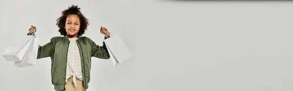 A young boy confidently holds shopping bags in front of a white background. — Stock Photo