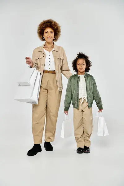 Curly African American mother and daughter in stylish clothes hold shopping bags against a white background. — Stock Photo