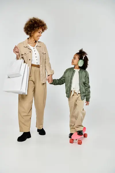 Curly African American mother and daughter in stylish clothes hold shopping bags and hands against a white background. — Stock Photo