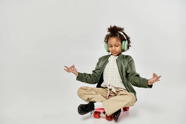A stylish curly African American girl sitting on a skateboard, wearing headphones. — Stock Photo