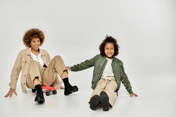 Curly African American mother and daughter in stylish clothes bonding while sitting on the floor with a skateboard. — Stock Photo