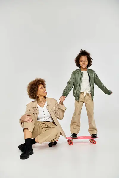 Curly African American mother and daughter in stylish clothes enjoy a fun skateboarding session together on a grey background. — Stock Photo