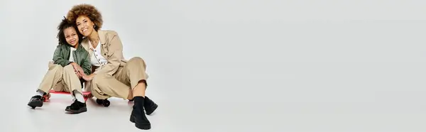 A curly African American mother and daughter in stylish clothes, sitting gracefully on a white background. — Stock Photo