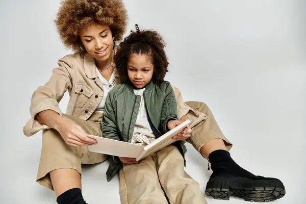 A curly African American mother and daughter sit on the floor, engrossed in a book, sharing a special moment of reading together. — Stock Photo