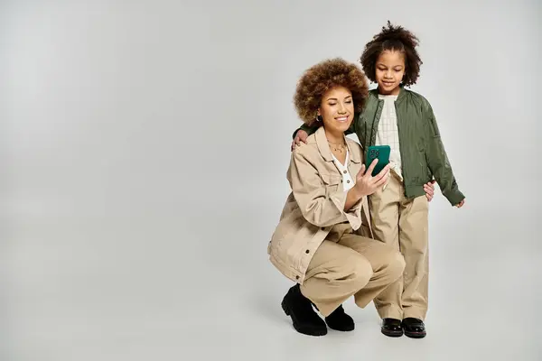 Un riccio afroamericano madre e figlia in abiti eleganti colpisce una posa insieme su uno sfondo grigio. — Foto stock