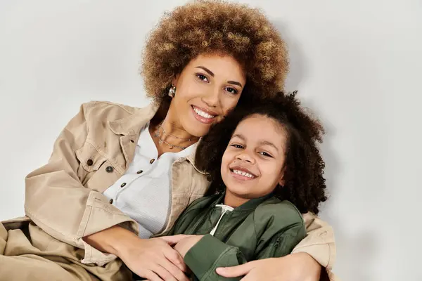 Curly African American mother and daughter in stylish clothes posing together on a grey background. — Stock Photo