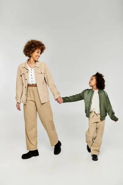 A curly African American mother and daughter in stylish clothes holding hands against a white background. — Stock Photo