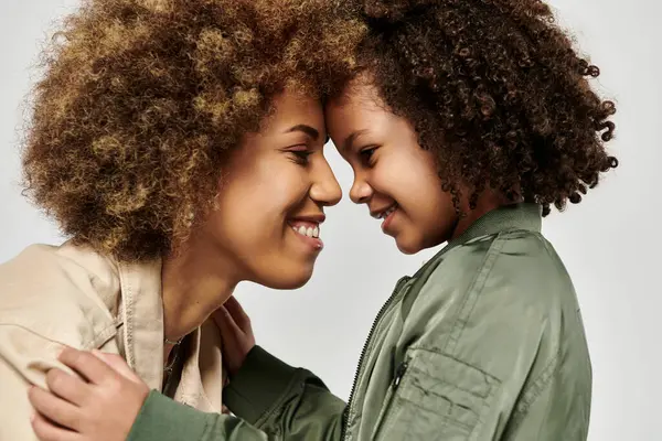 A curly African American mother and daughter, dressed in stylish clothes, share a heartfelt hug against a white background. — Stock Photo