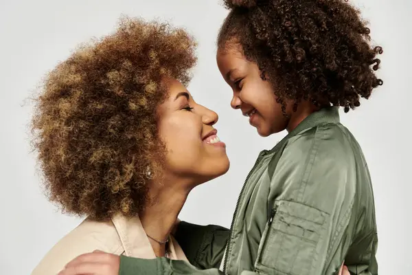 An African American mother and daughter, both with curly hair, sharing a loving hug against a gray backdrop. — Stock Photo