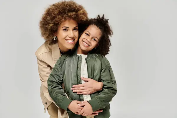 Curly African American mother and daughter in stylish clothes sharing a warm hug against a gray backdrop. — Stock Photo