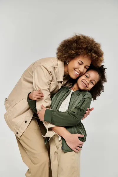 Lockige afroamerikanische Mutter und Tochter umarmen sich liebevoll in stilvoller Kleidung vor weißem Hintergrund. — Stockfoto