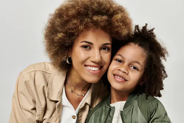 A stylish African American mother with curly afro hair and her little girl posing on a grey background. — Stock Photo