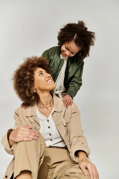A curly African American mother and daughter in stylish clothes sitting together on a white background. — Stock Photo