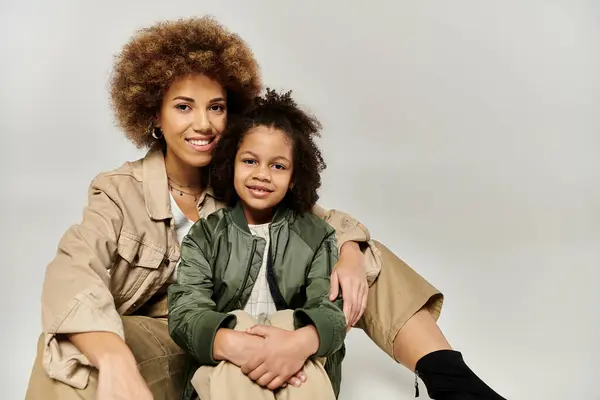 An African American mother and her curly-haired daughter, dressed in stylish clothes, striking a pose on a grey background. — Stock Photo