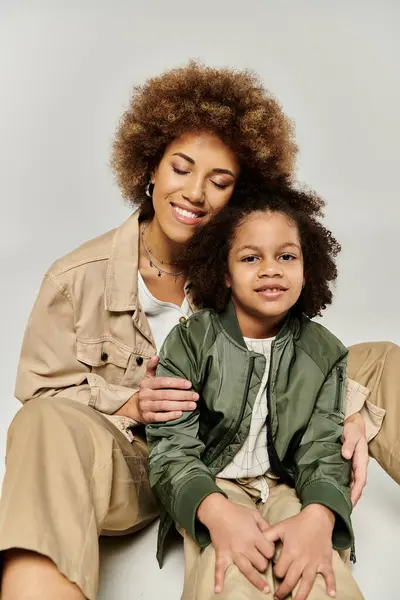 A curly African American mother and daughter, dressed stylishly, posing for the camera against a grey background. — Stock Photo