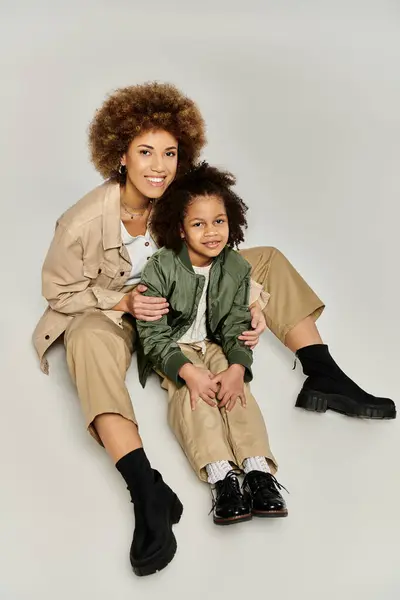 Curly African American mother and daughter in stylish clothes pose elegantly against a grey background. — Stock Photo