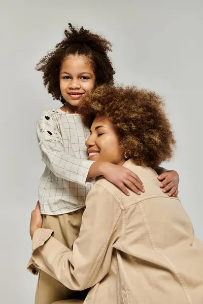 Curly African American mother and daughter in stylish clothes sharing a heartwarming hug on a gray background. — Stock Photo