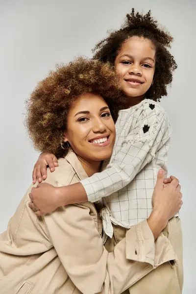 Curly African American mother and daughter in stylish clothes hugging lovingly against a gray background. — Stock Photo