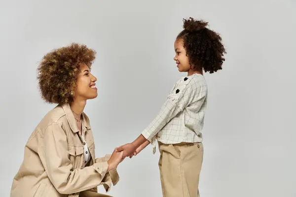 Curly African American mother and daughter holding hands in stylish clothes against a grey background. — Stock Photo