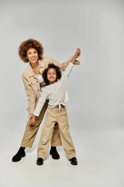 A curly African American mother and daughter in stylish clothes striking a pose on a grey background. — Stock Photo