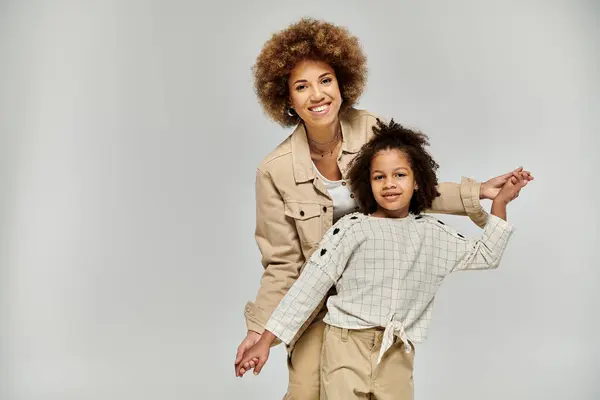 A curly African American mother and daughter, in stylish clothing, striking a pose on a grey background. — Stock Photo