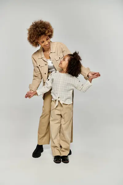 A curly African American mother and daughter stand confidently in front of a white background, showcasing their stylish outfits. — Stock Photo