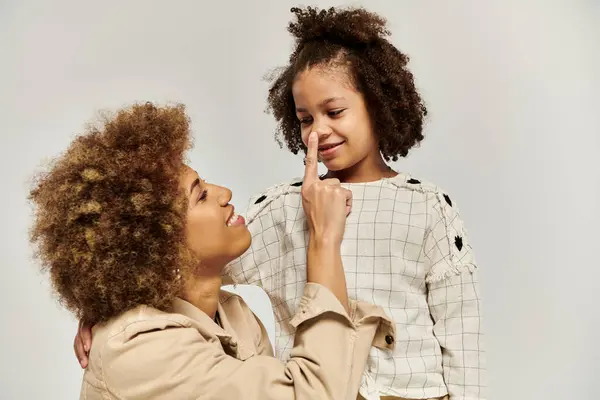 A curly African American mother touching nose of daughter in stylish attire against a grey backdrop. — Stock Photo