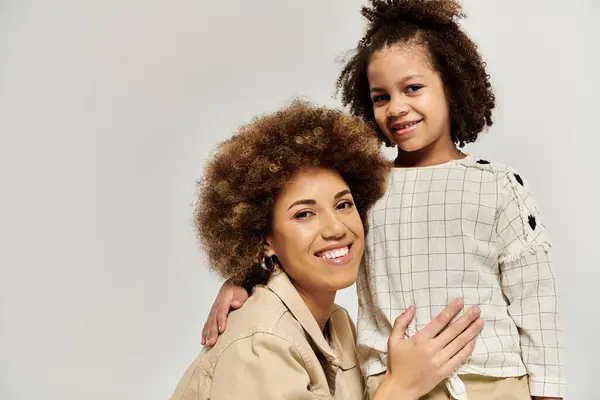Curly African American mother and daughter in fashionable attire, striking a pose together on a chic grey backdrop. — Stock Photo