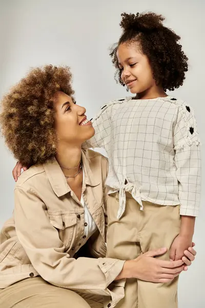 Stylish curly African American mother and daughter striking a pose together on a grey background. — Stock Photo