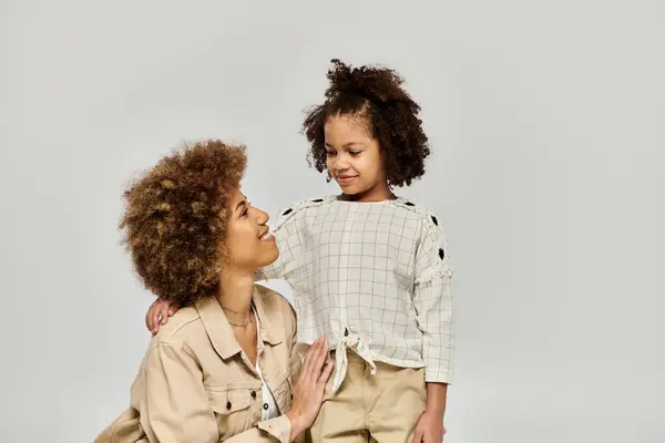 A curly African American mother and daughter in stylish clothes posing gracefully on a grey background. — Stock Photo