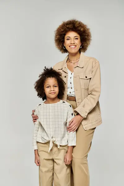 Mãe e filha afro-americana de cabelos encaracolados fazem uma pose elegante contra um pano de fundo cinza neutro. — Fotografia de Stock