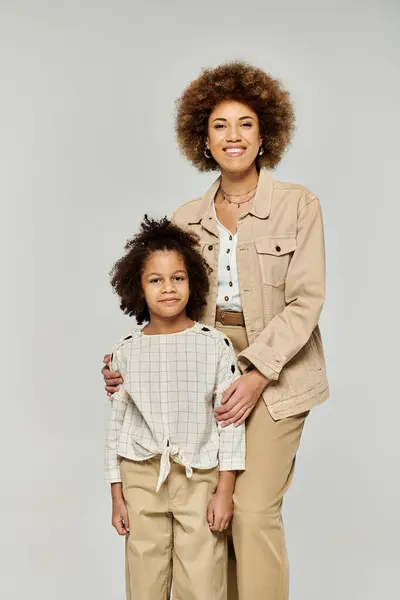 Curly-haired African American mother and daughter strike a stylish pose against a neutral grey backdrop. — Stock Photo