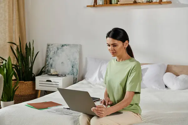 Uma mulher em traje casual senta-se em uma cama, imersa em seu trabalho laptop. — Fotografia de Stock