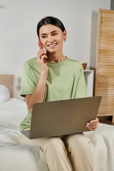 Woman in casual attire talks on phone while sitting on bed. — Stock Photo