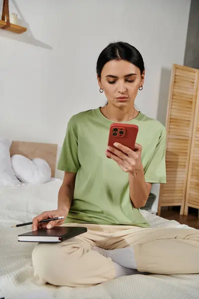 A woman in casual attire sits on a bed, focused on her cell phone screen. — Stock Photo