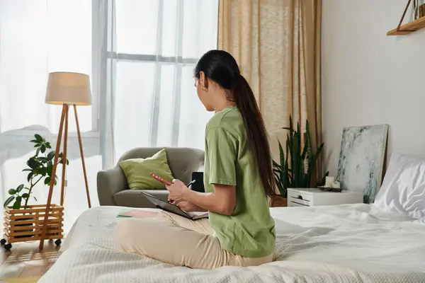 A woman in casual attire perched on a bed next to a window. — Stock Photo