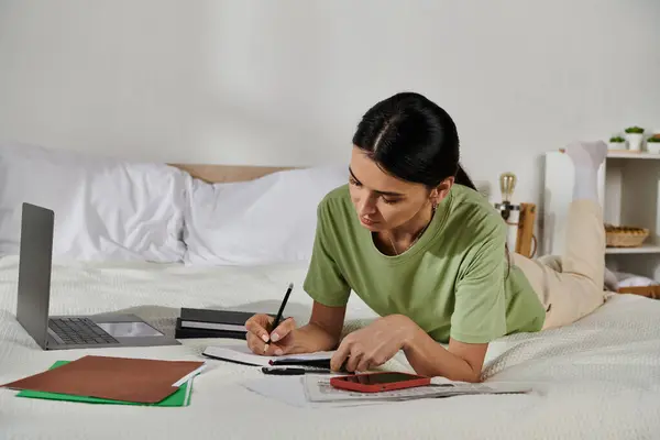 A woman in casual attire lays on a bed, writing in a notebook. — Stock Photo
