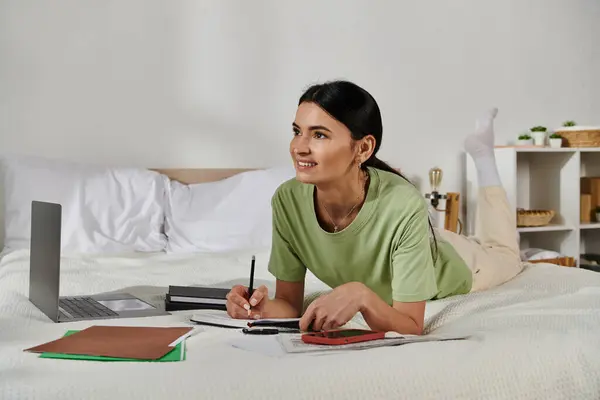 Donna in abbigliamento casual rilassante sul letto, scrivendo sul taccuino. — Foto stock