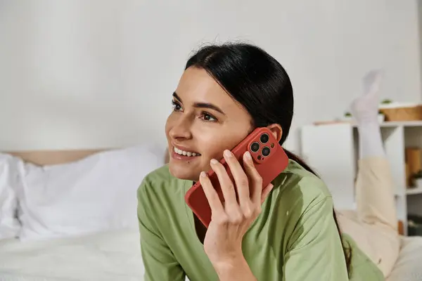 Woman in casual attire talking on cell phone while reclining on bed. — Stock Photo