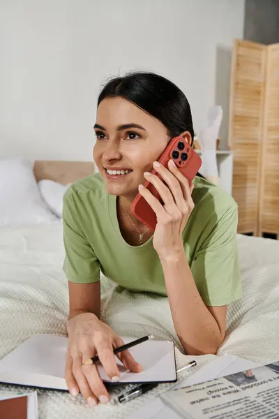 Woman in casual attire lounging on a bed while chatting on a cell phone. — Stock Photo