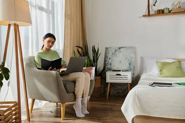 Woman sits, focused on laptop and book while working from home. — Stock Photo