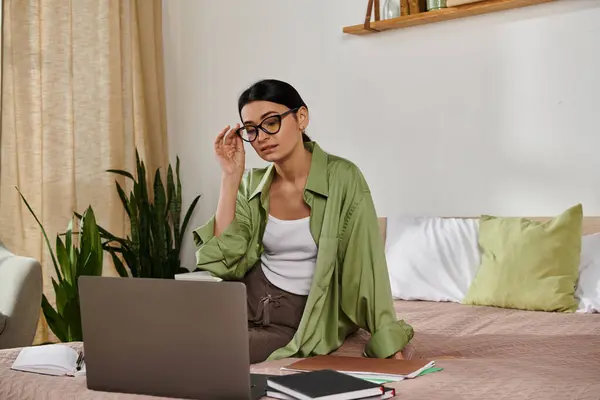 Woman in casual attire sitting on bed, working on laptop. — Stock Photo