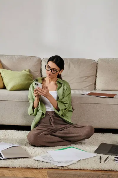 A woman in casual attire sitting on the floor absorbed in her cell phone. — Stock Photo