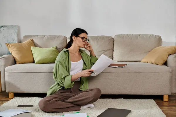 Una donna in abbigliamento casual siede sul pavimento, assorta nella lettura di un giornale. — Foto stock