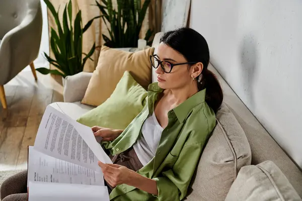 A woman in casual attire sitting on a couch engrossed in reading paperwork. — Stock Photo