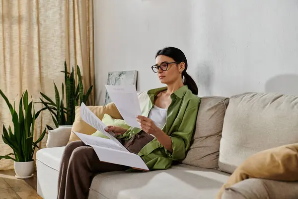 A woman in casual attire sits on a couch, reading a paper. — Stock Photo